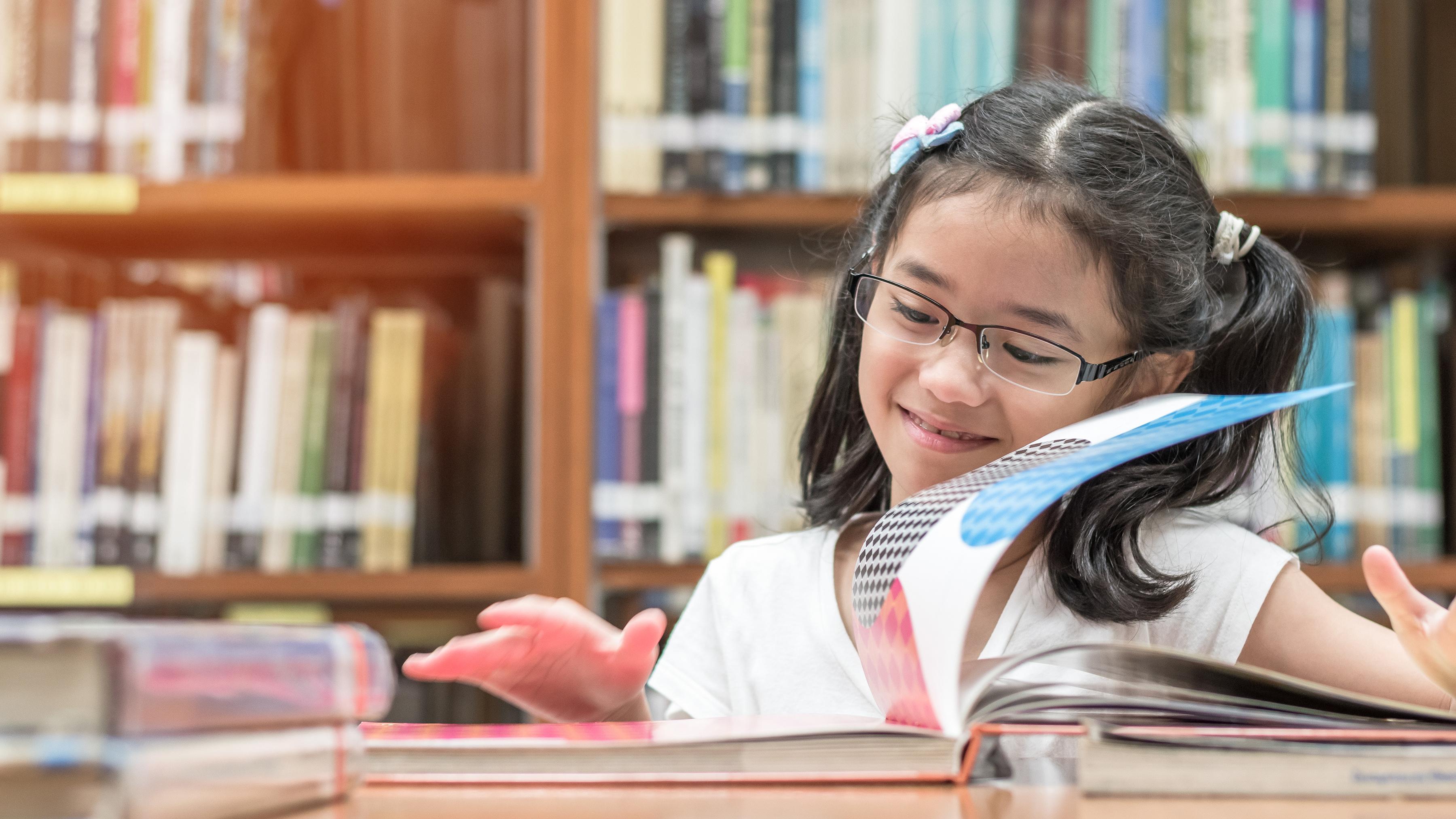Happy girl reading a book in a library
