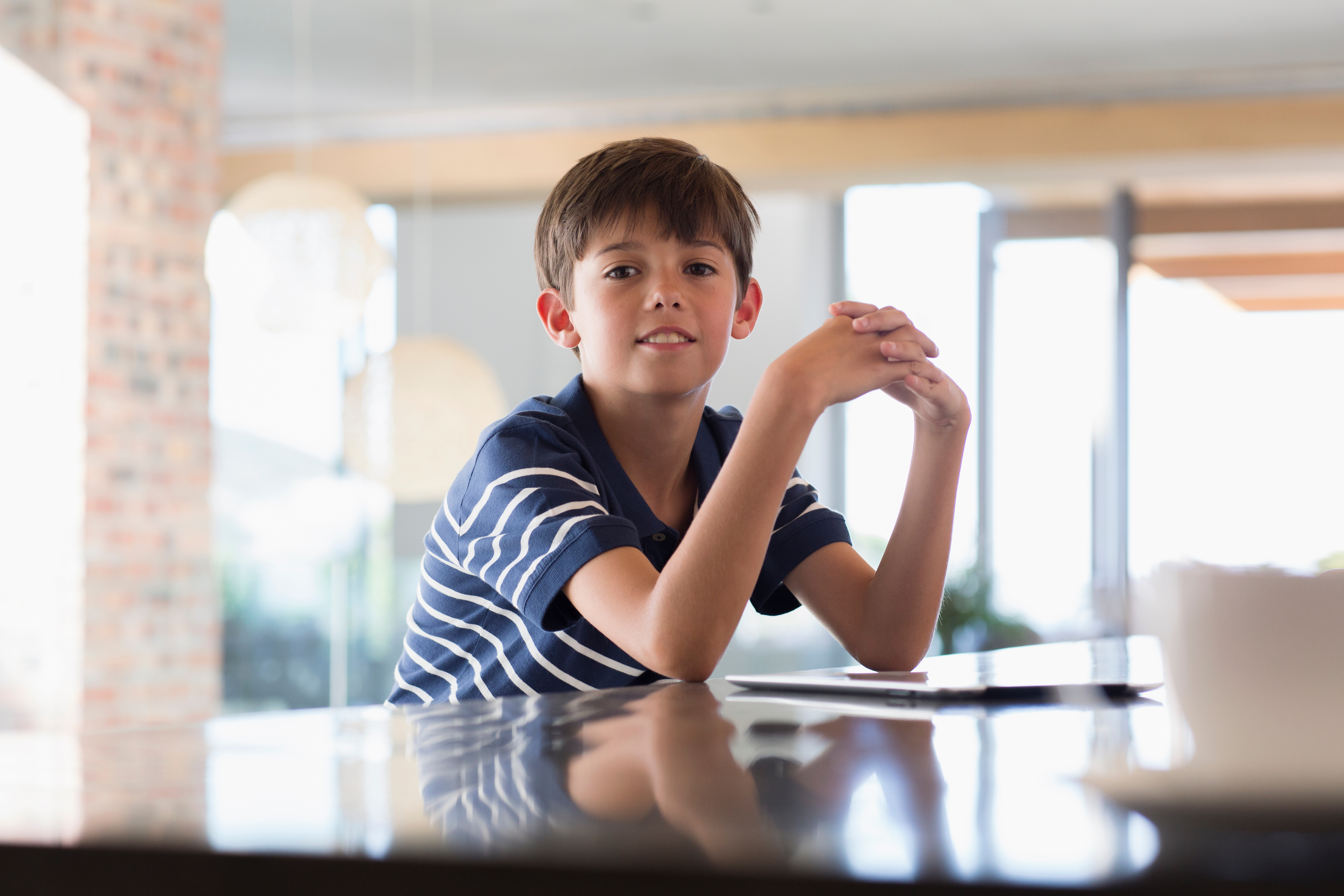 A young boy sits at a kitchen counter, focused on a tablet, representing how children commonly use devices in everyday home settings.